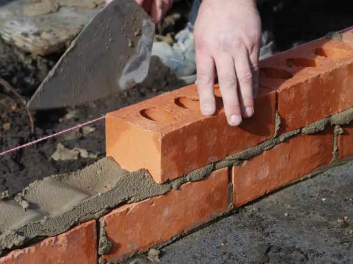 Bricklayer making brick wall weep holes during construction .
